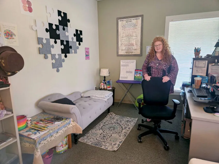 Professional female with red curly hair standing in her comfortably decorated office with artwork on the walls.