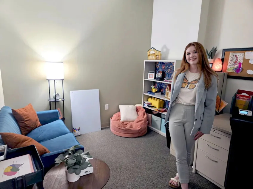 Young female professional wearing a light blue suit with a butterfly t-shirt and standing in her office decorated with tasteful and calming colors.