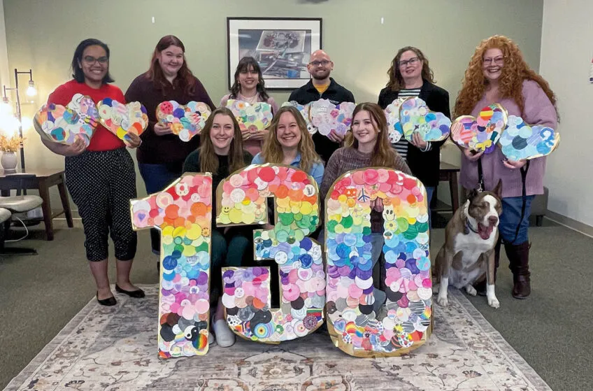 staff photo in two rows with three seated in front holding a 1, a 3, and a 0 in celebration of Cunningham's anniversary